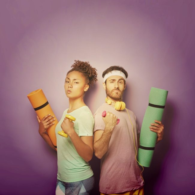 Une femme et un homme diversifiés sérieux et confiants se reculent, lèvent les bras avec des haltères